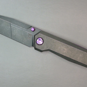 A modern, sleek folding knife with a metallic finish and purple accents.