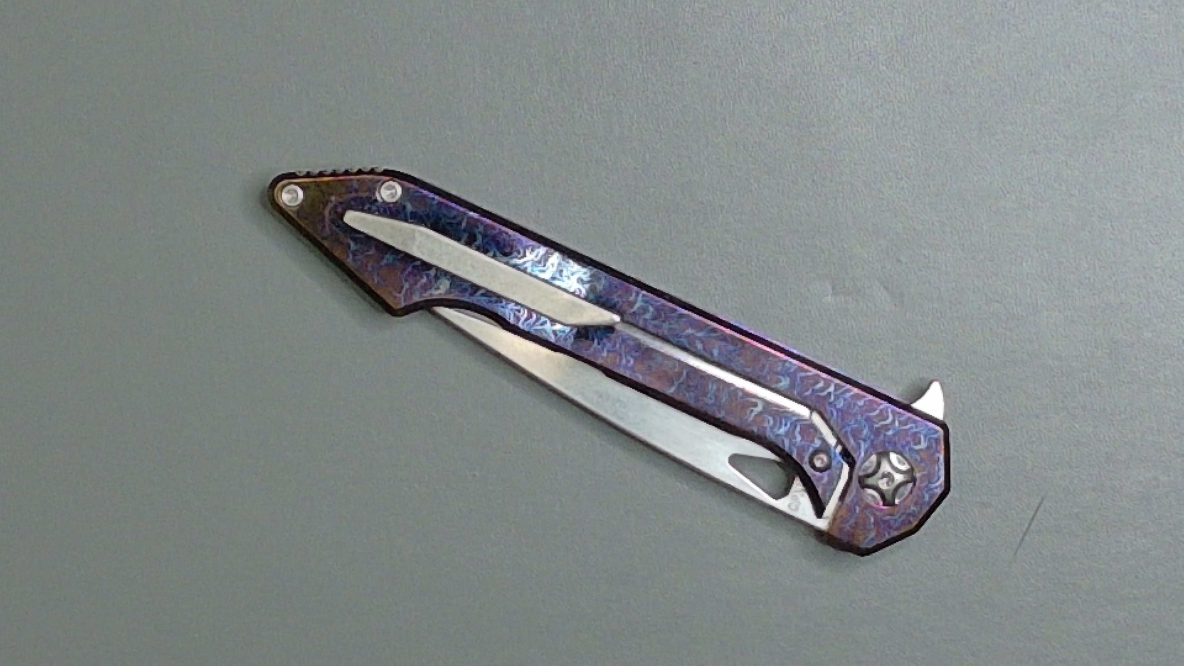 A sleek purple folding knife with a clip on a gray surface.