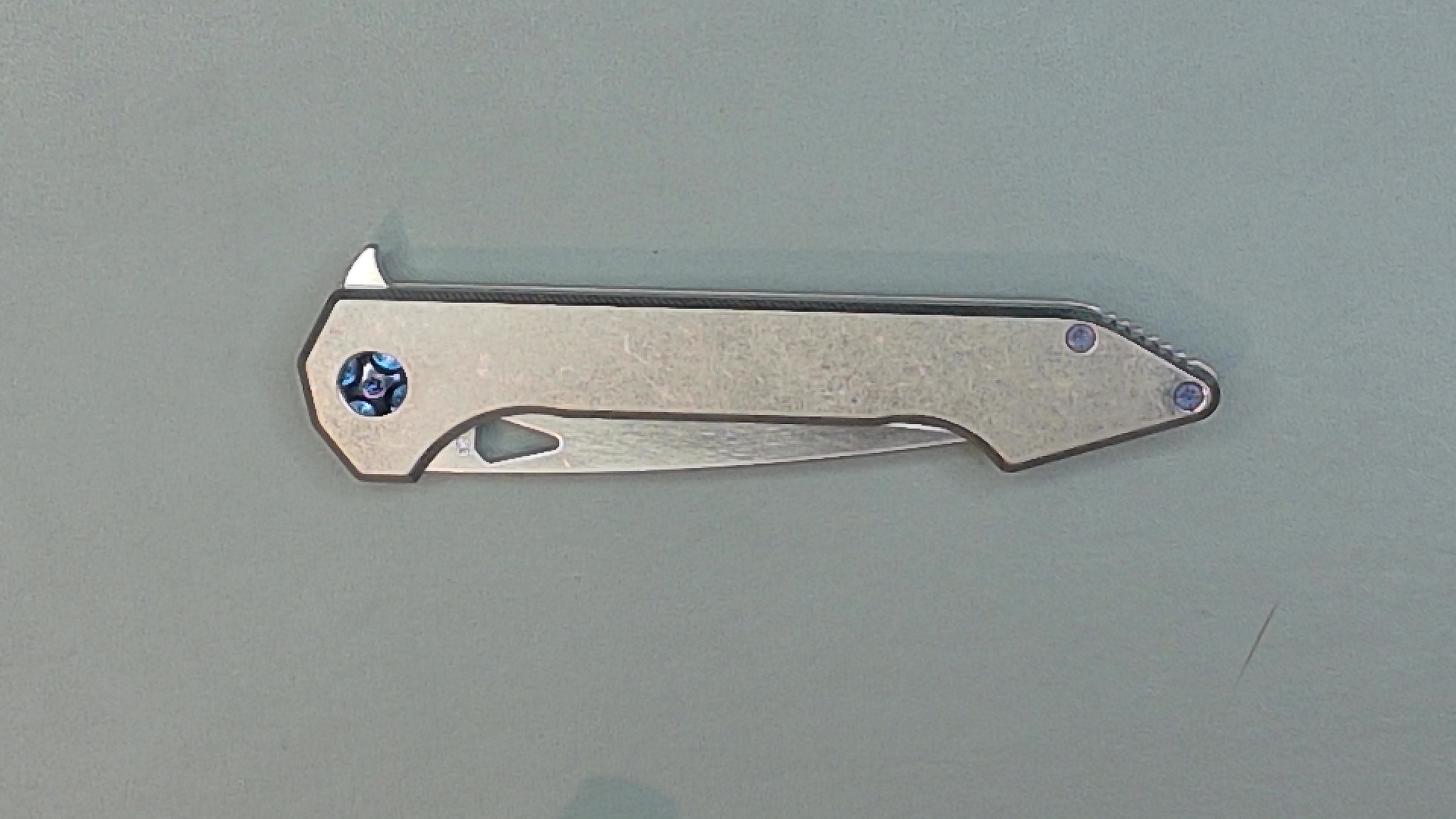 Folded pocket knife with a metallic handle on a gray surface.