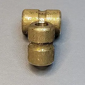 A brass T-shaped pipe fitting with detailed engravings.