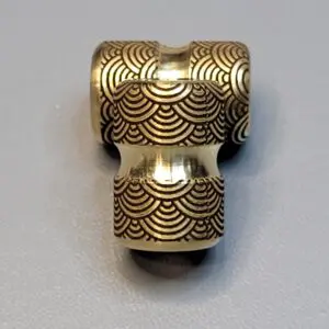 Intricately designed metal T-shaped pipe fitting with engraved wave patterns.