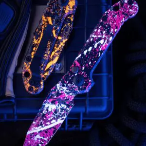 Microtech LUDT Gen III T/E automatic knife closed, Black handle, Bull Shark Gray and Orange splatter blade under UV light